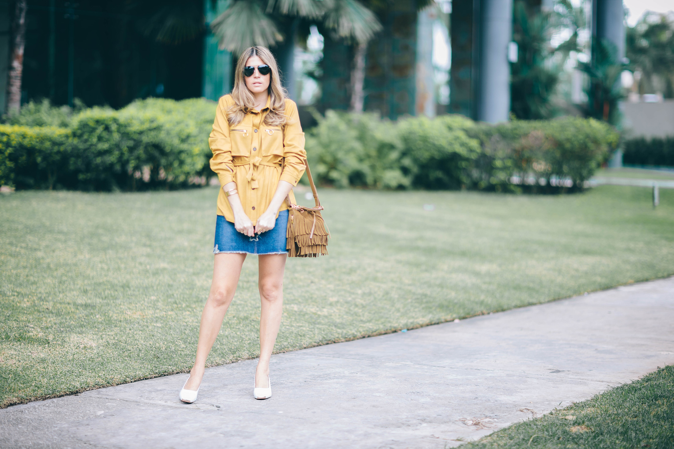 A Constellation blogger wears a suede belted jacket, denim skirt, slingback shoes and fringe bucket bag with aviator sunglasses