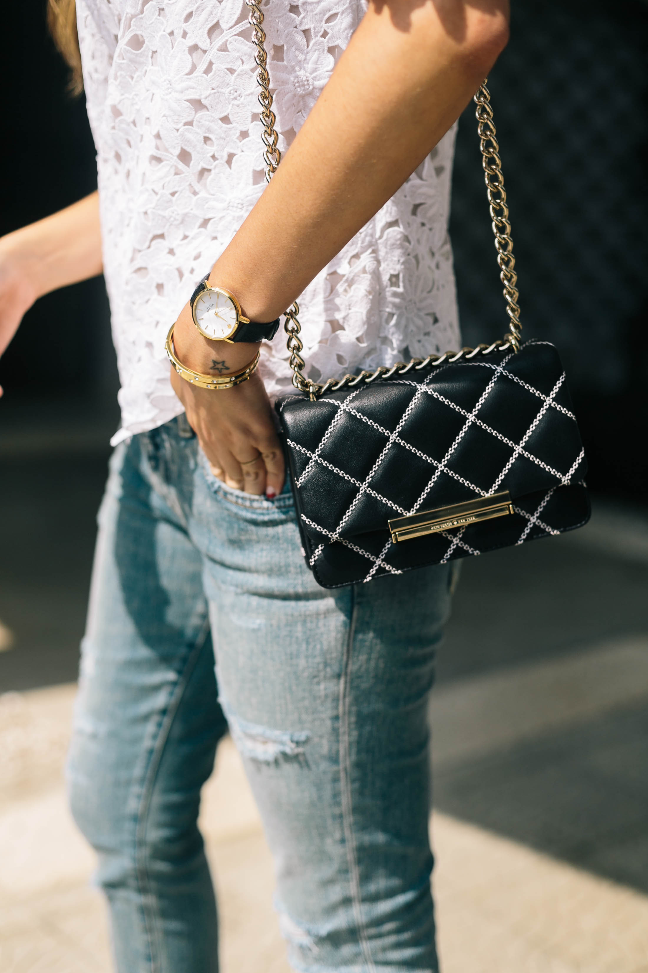 Maristella's outfit details: lace, denim, black leather quilted shoulder bag, minimalist watch and gold bangles over a dainty star tattoo
