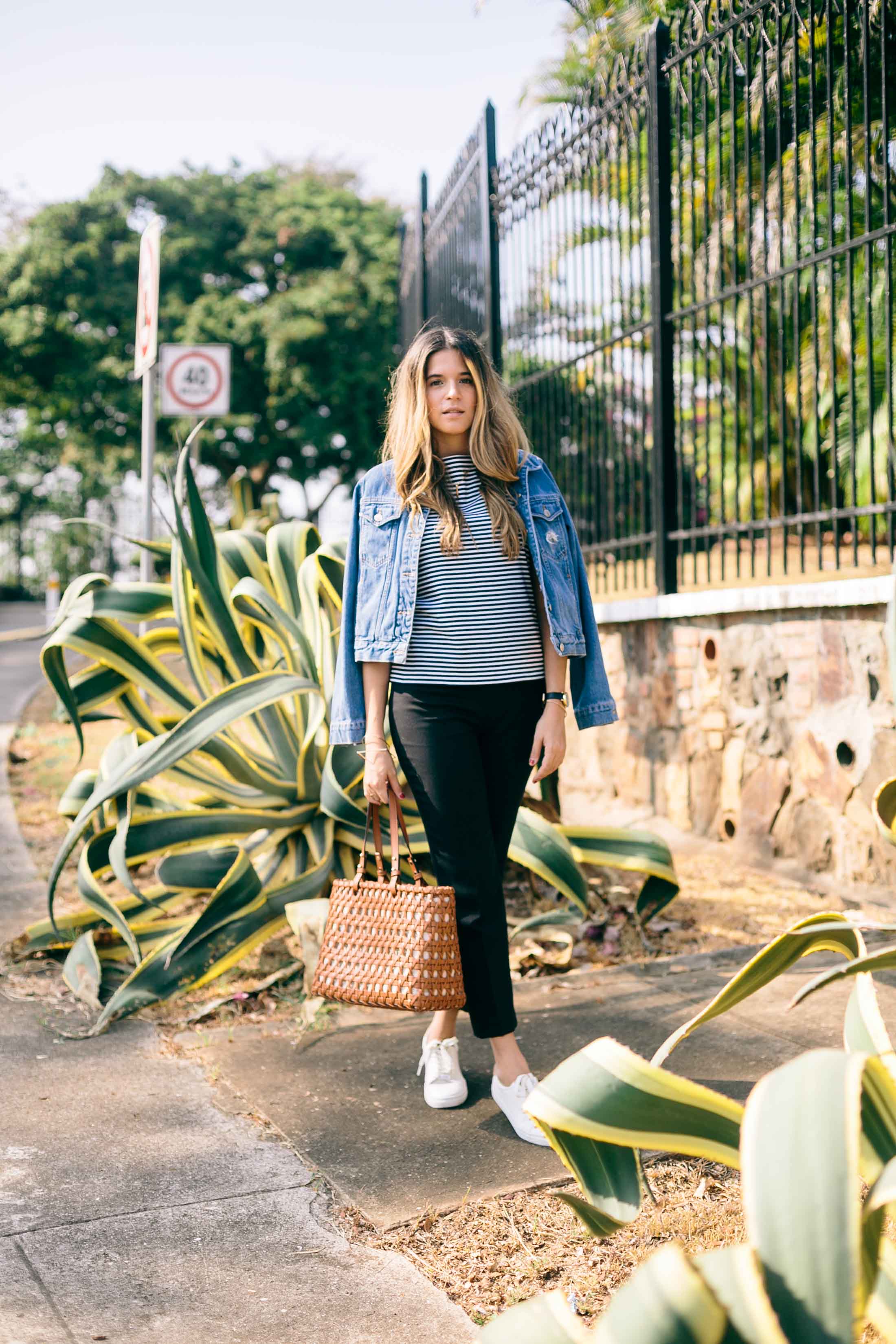Maristella wears a casual and easy everyday outfit with a striped t-shirt, black skinny pants, white sneakers, denim jacket and tan leather tote bag.