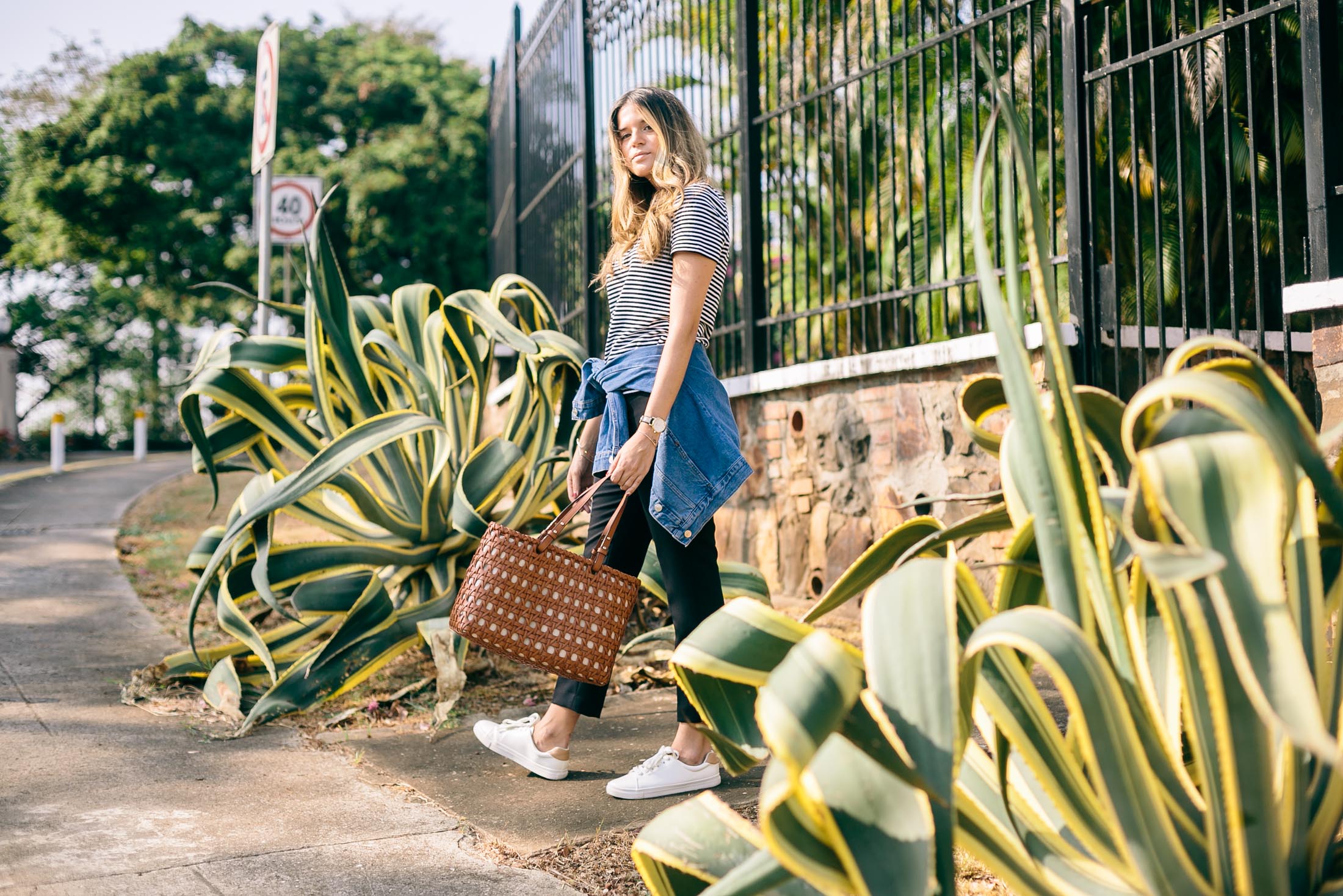 Maristella in a chic effortless everyday outfit with a striped t-shirt, black skinny pants, white sneakers, tan leather tote bag and jean jacket