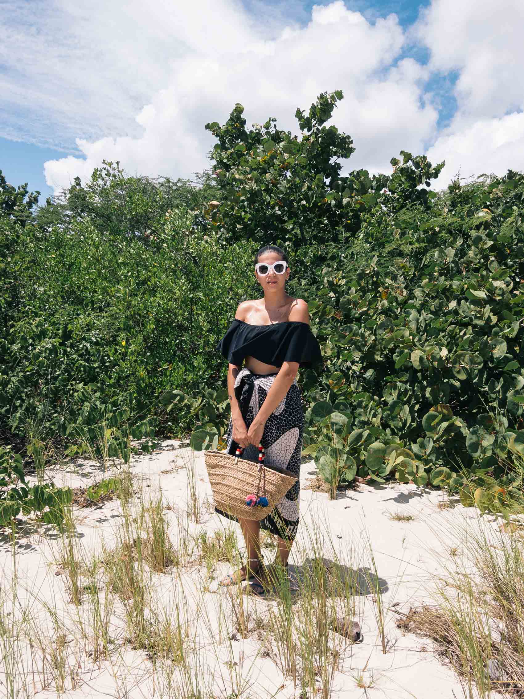 Maristella wears Celine sunglasses, off shoulder black bikini and straw tote bag. Vacation style, beach style, summer style, island style