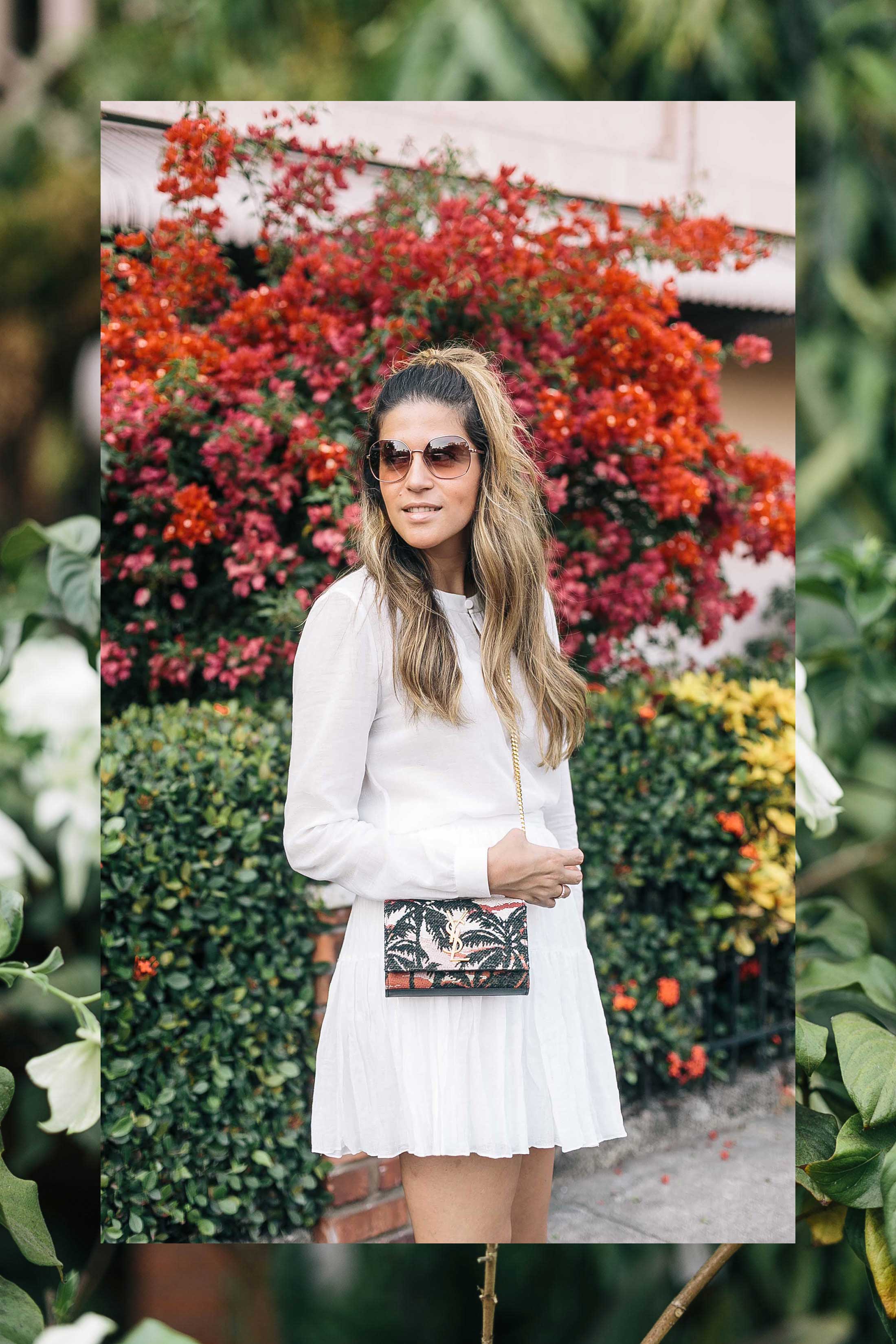 Maristella wears pink sunglasses from Kate Spade, white blouse, white skirt and palm print bag from Saint Laurent