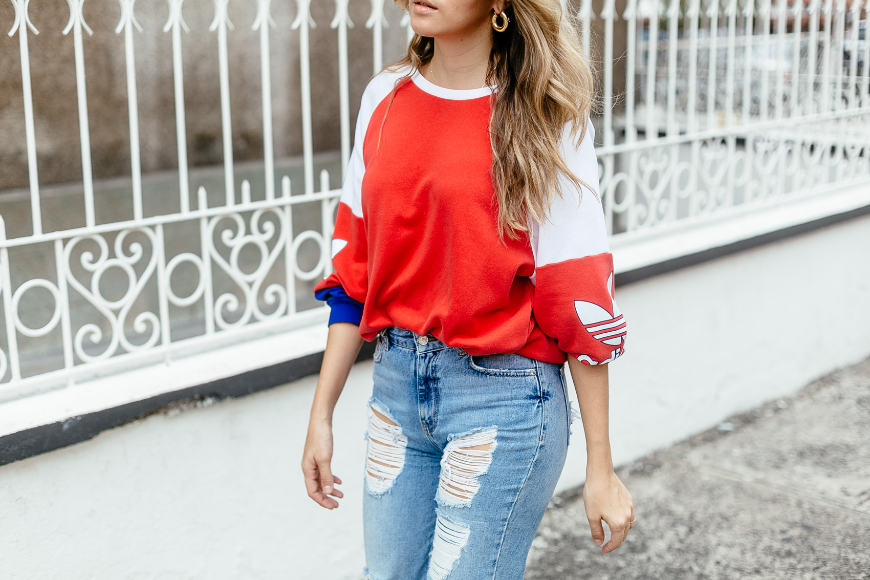 Maristella wearing statement gold earrings, an adidas jumper and ripped jeans