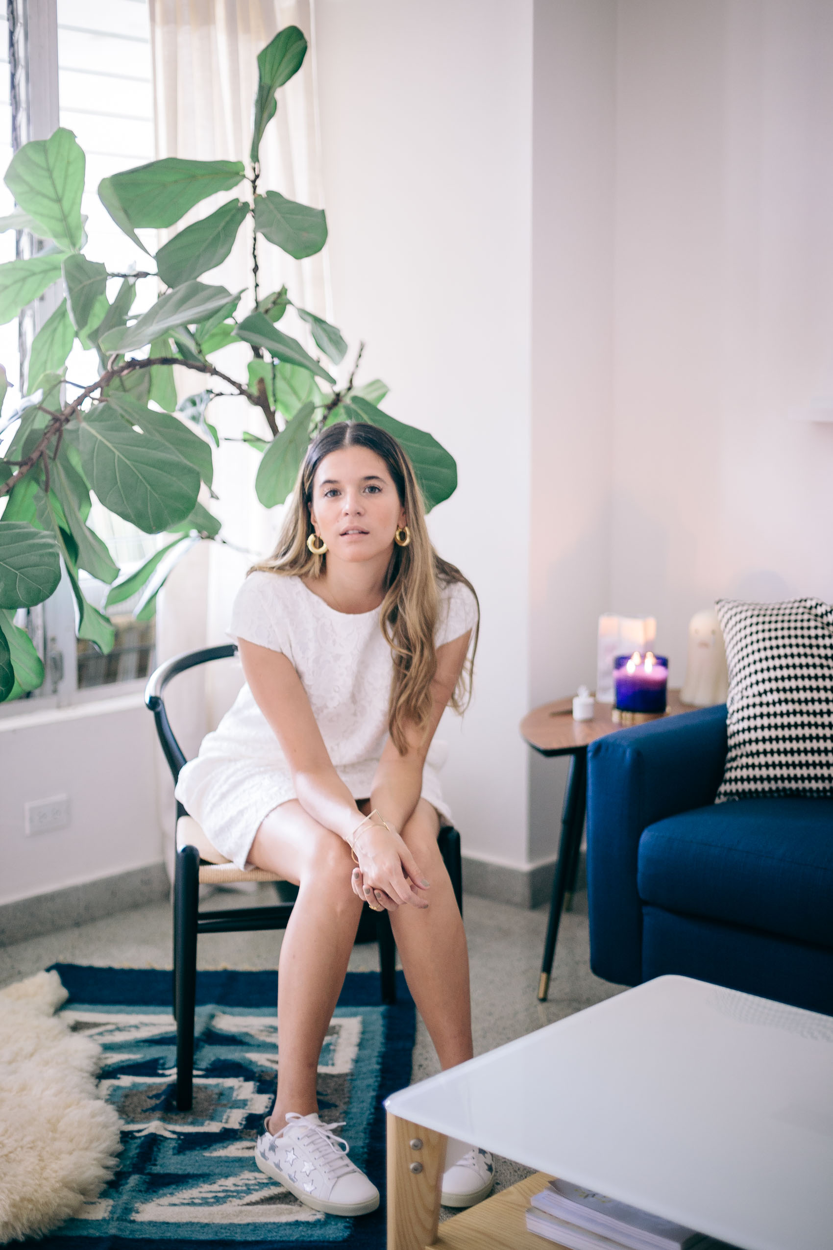 Blogger Maristella Gonzalez at her home in Panama wearing Saint Laurent sitting in a wishbone chair over a sheepskin rug, wool rug from Guatemala and fiddle leaf fig tree in the back