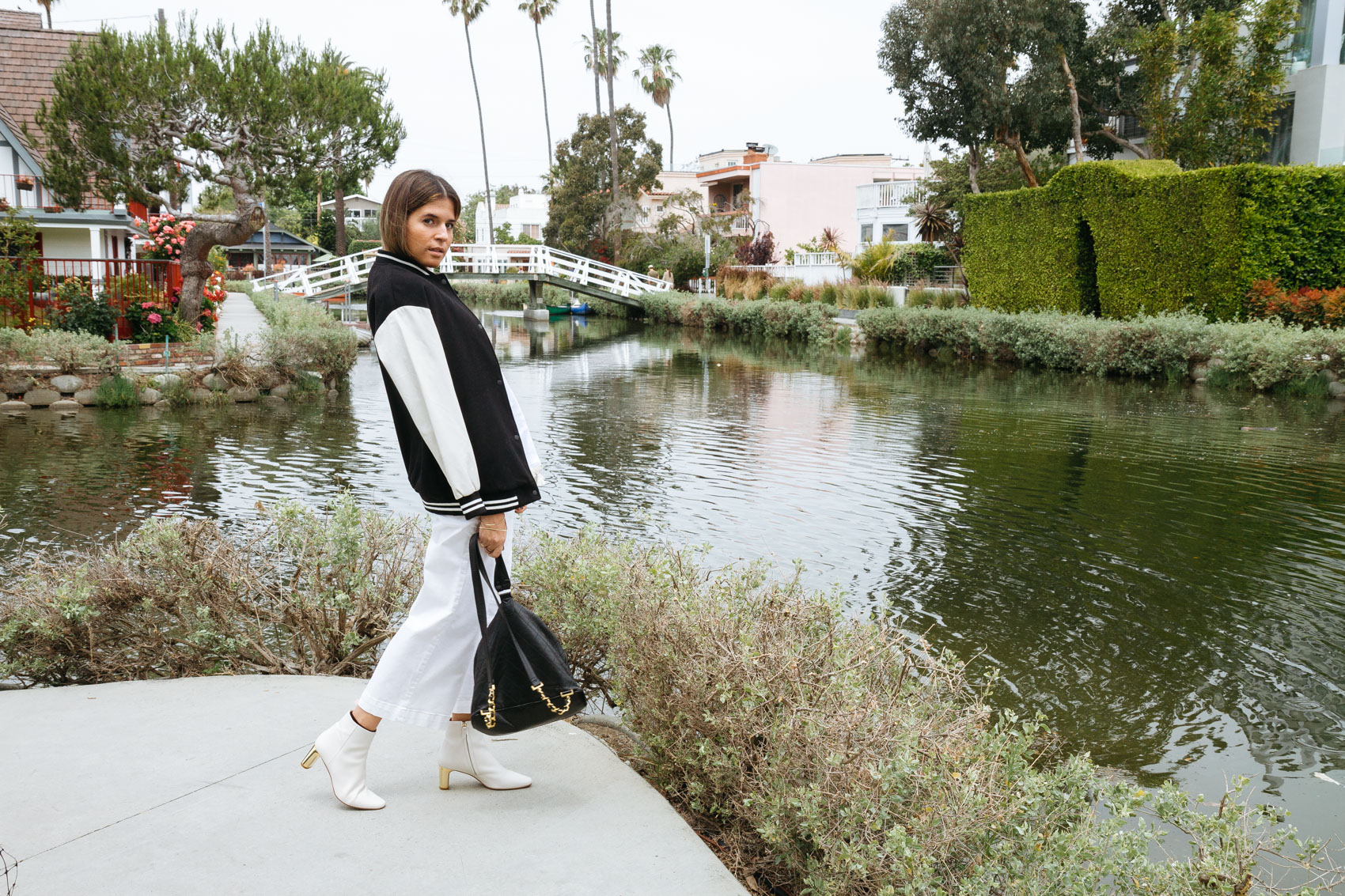 Blogger Maristella in California wearing a black and white varsity bomber jacket, white flared cropped jeans, white ankle boots and vintage Chanel backpack