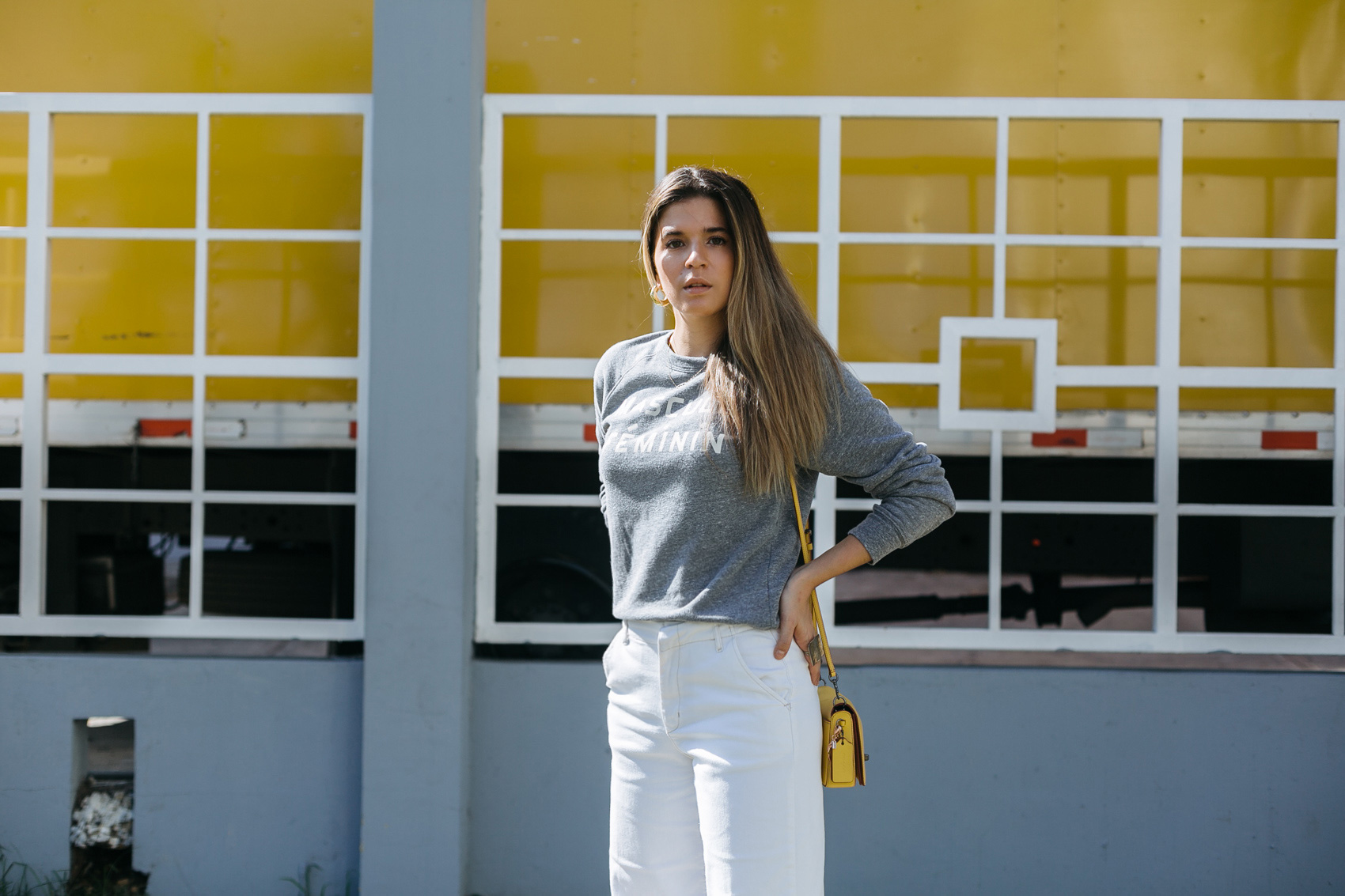 Maristella wearing a grey sweatshirt with white jeans and yellow Coach Dinky bag