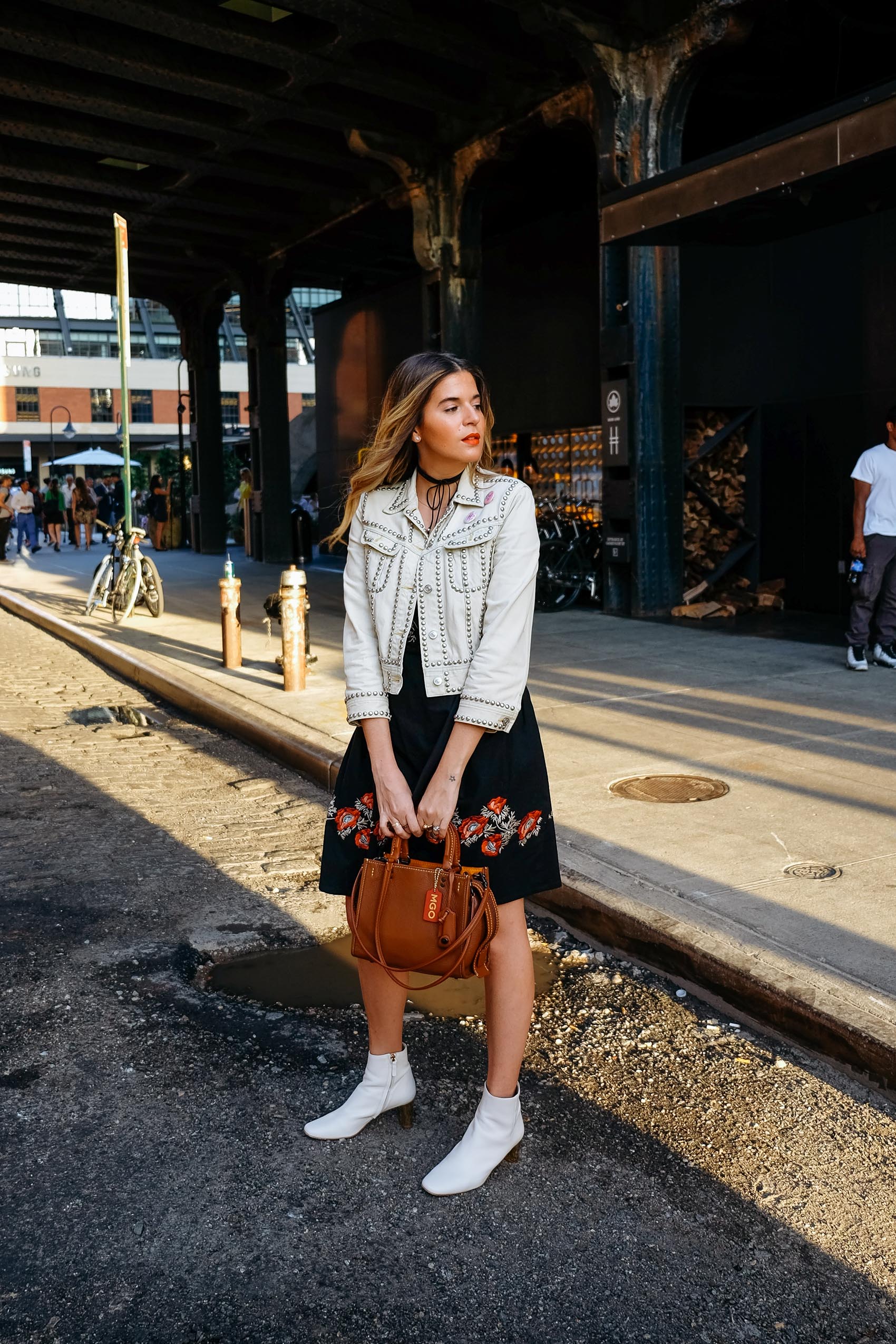 Maristella wears a studded ivory denim jacket from Coach, flower embroidered dress from H&M, white boots from Uterqüe, Coach Rogue bag in glovetan leather