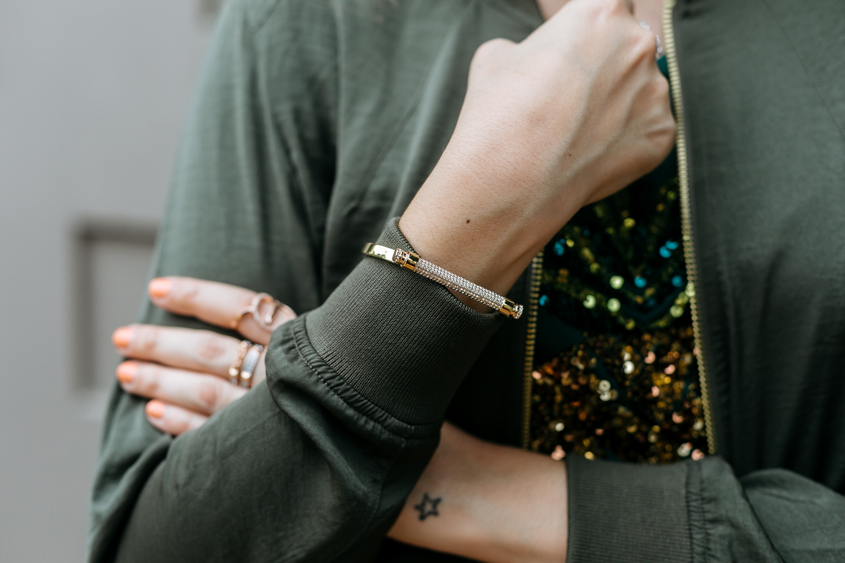 Swarovski bangle and rings, dainty star outline tattoo, army green satin bomber jacket and sequin t-shirt from H&M