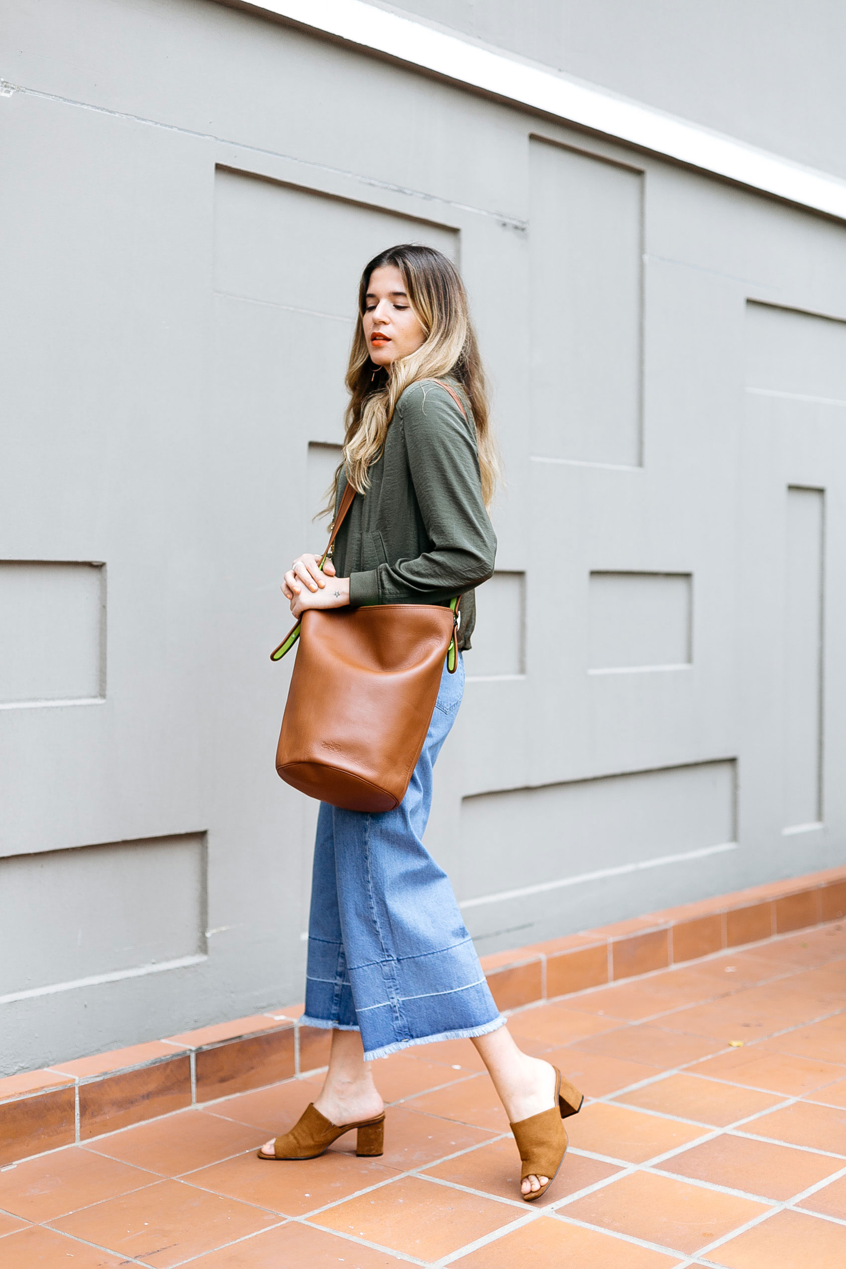 Maristella wearing a large Coach bucket bag, wide leg culottes with frayed hem, suede mules from Zara and green satin jacket from H&M