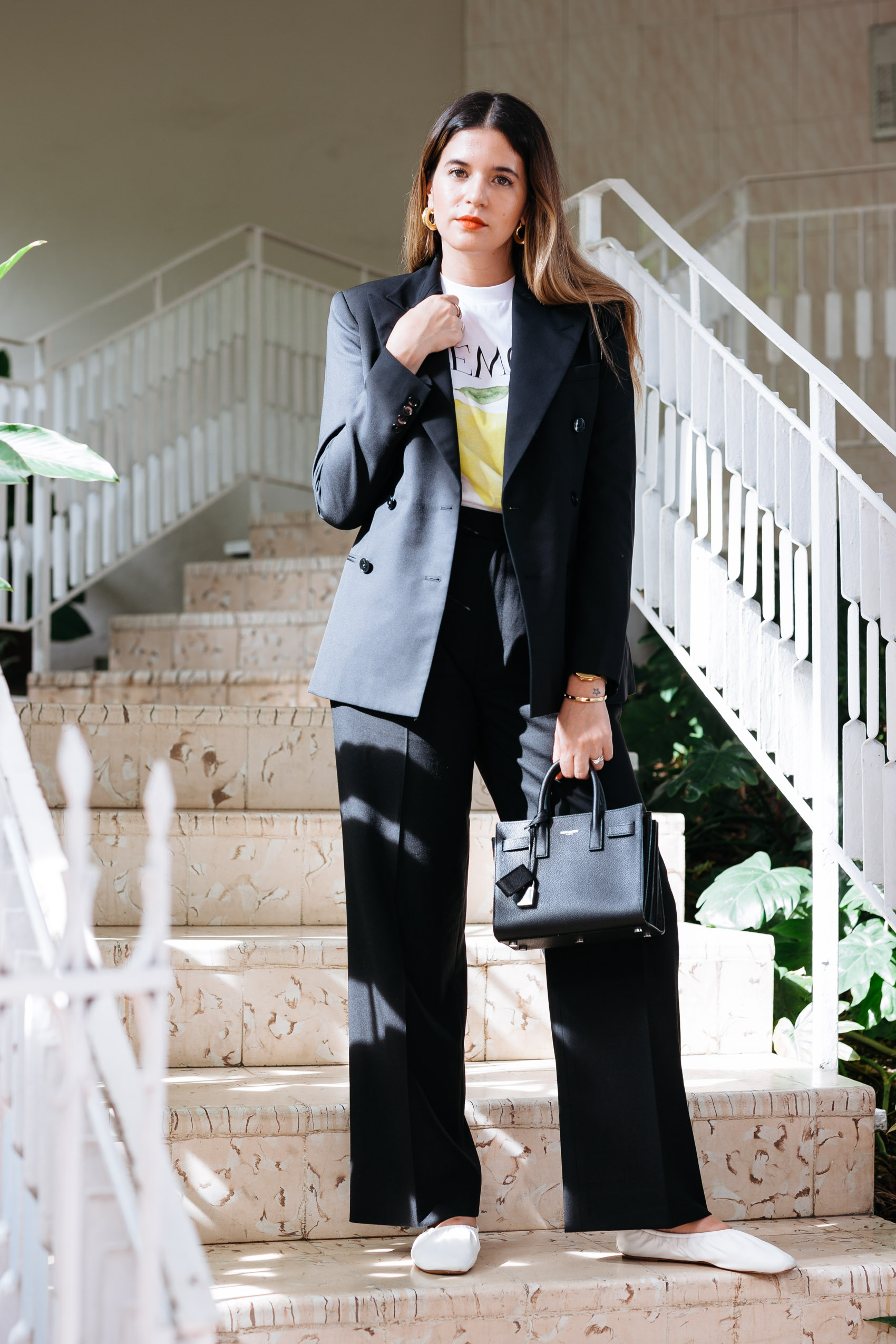 Maristella wears the Ganni lemon t-shirt with black trousers and double breasted blazer from Polo Ralph Lauren, Céline white leather flats, black nano Sac de Jour from YSL