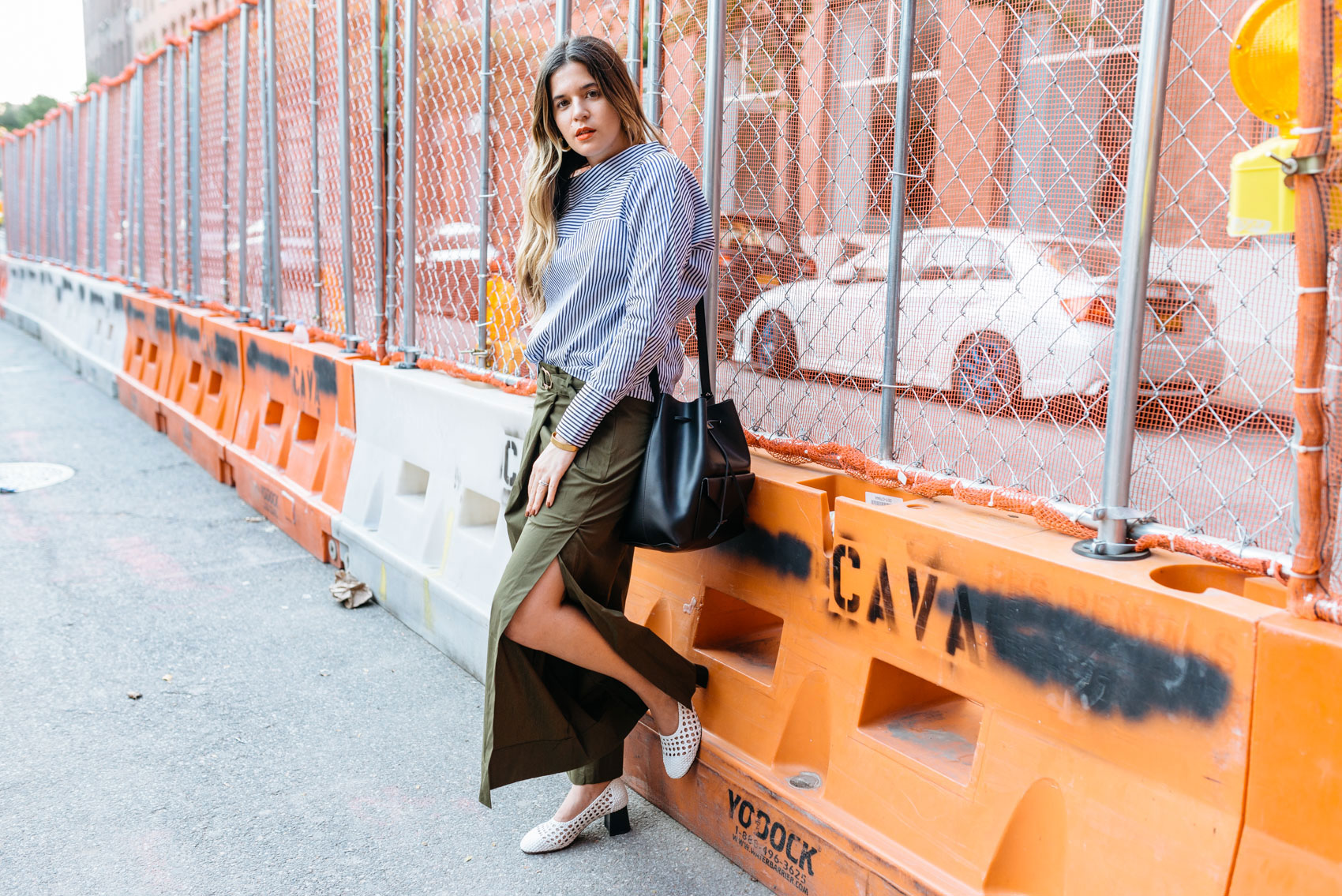 Maristella wearing a deconstructed open sleeve shirt, slit wide olive pants, Sandro braided shoes and a black bucket bag in NYFW