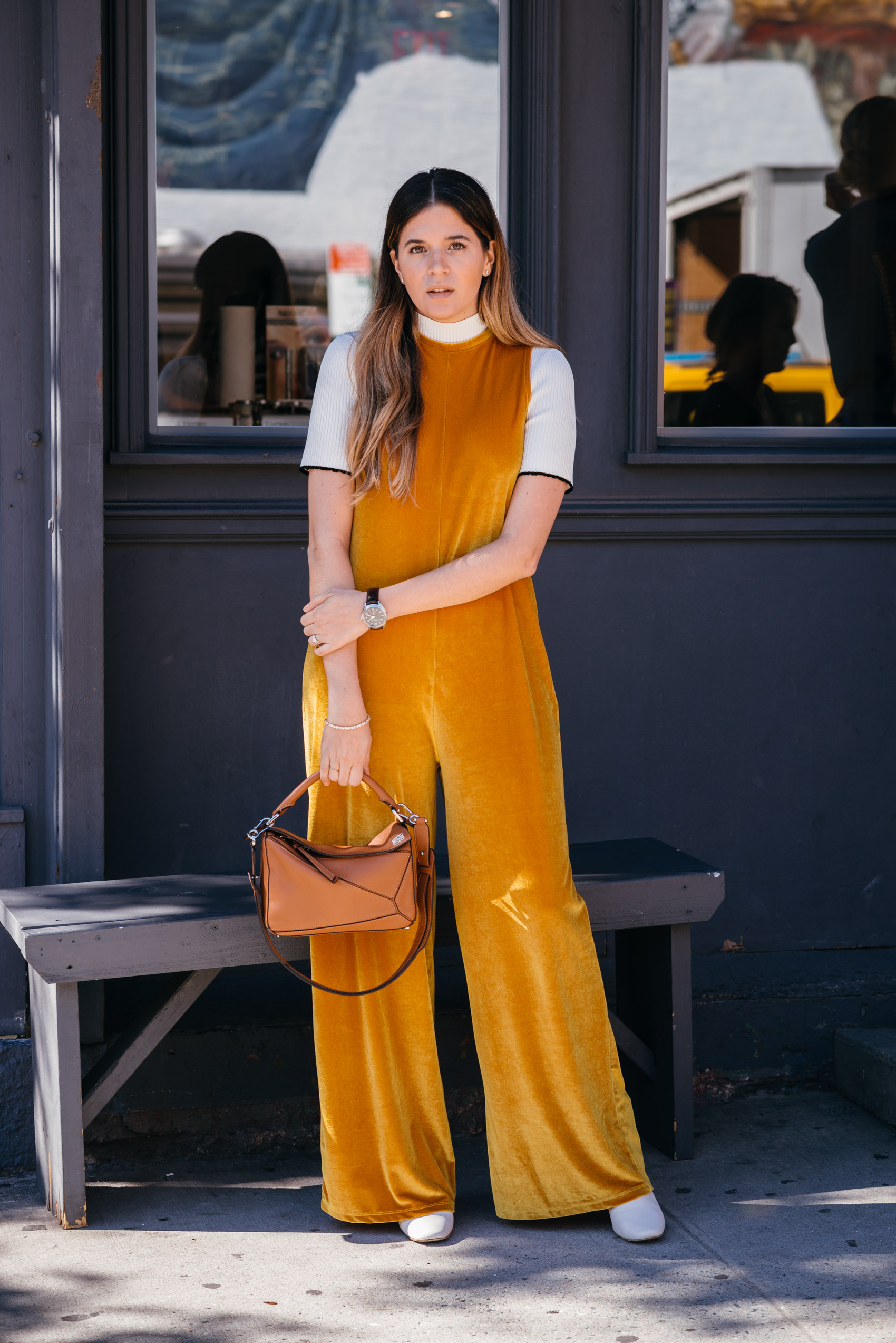 Maristella wearing a Zara TRF yellow velvet jumpsuit, contrast sleeves knit sweater, white boots and Loewe Puzzle bag in NYFW