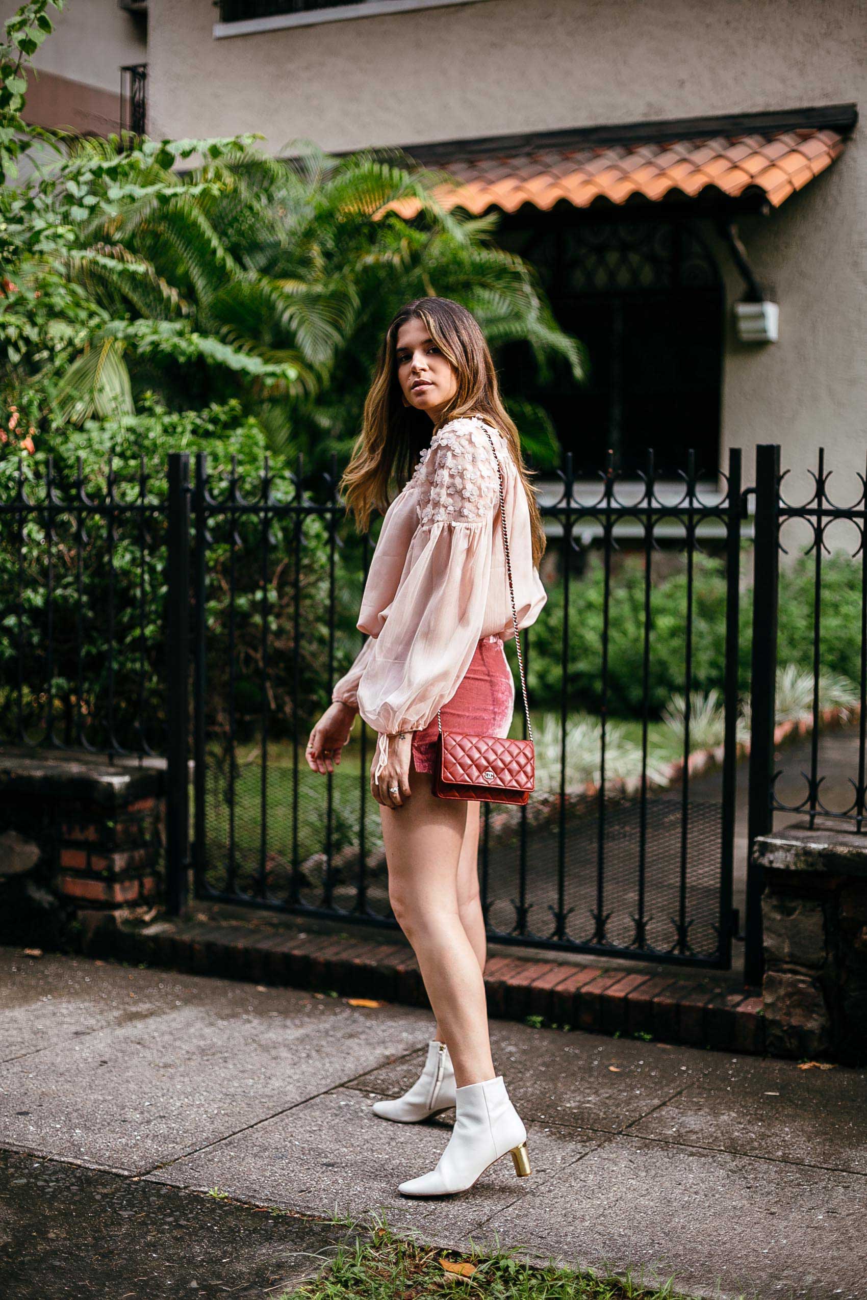 Maristella wearing a pink blouse, rose velvet shorts, white boots and red Chanel bag