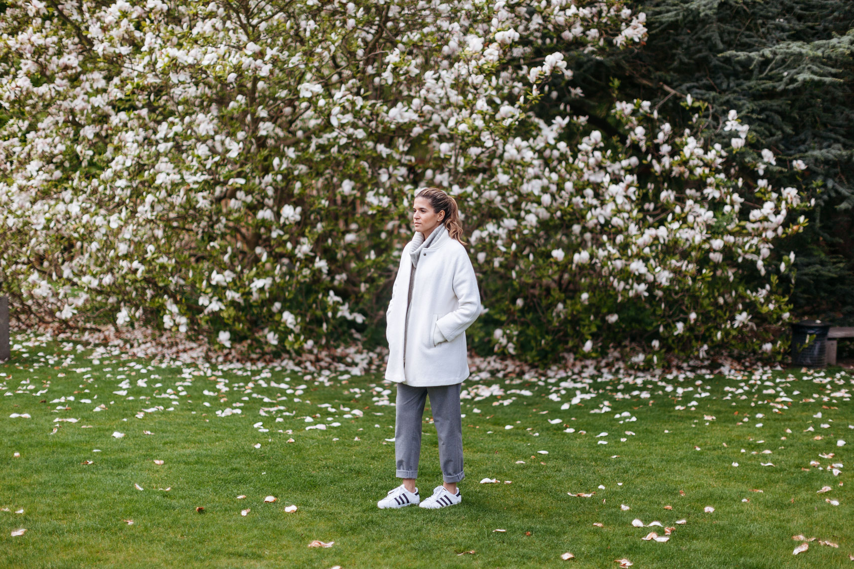 Maristella wearing a grey cashmere turtleneck, white coat, grey trousers and adidas Superstar black and white sneakers
