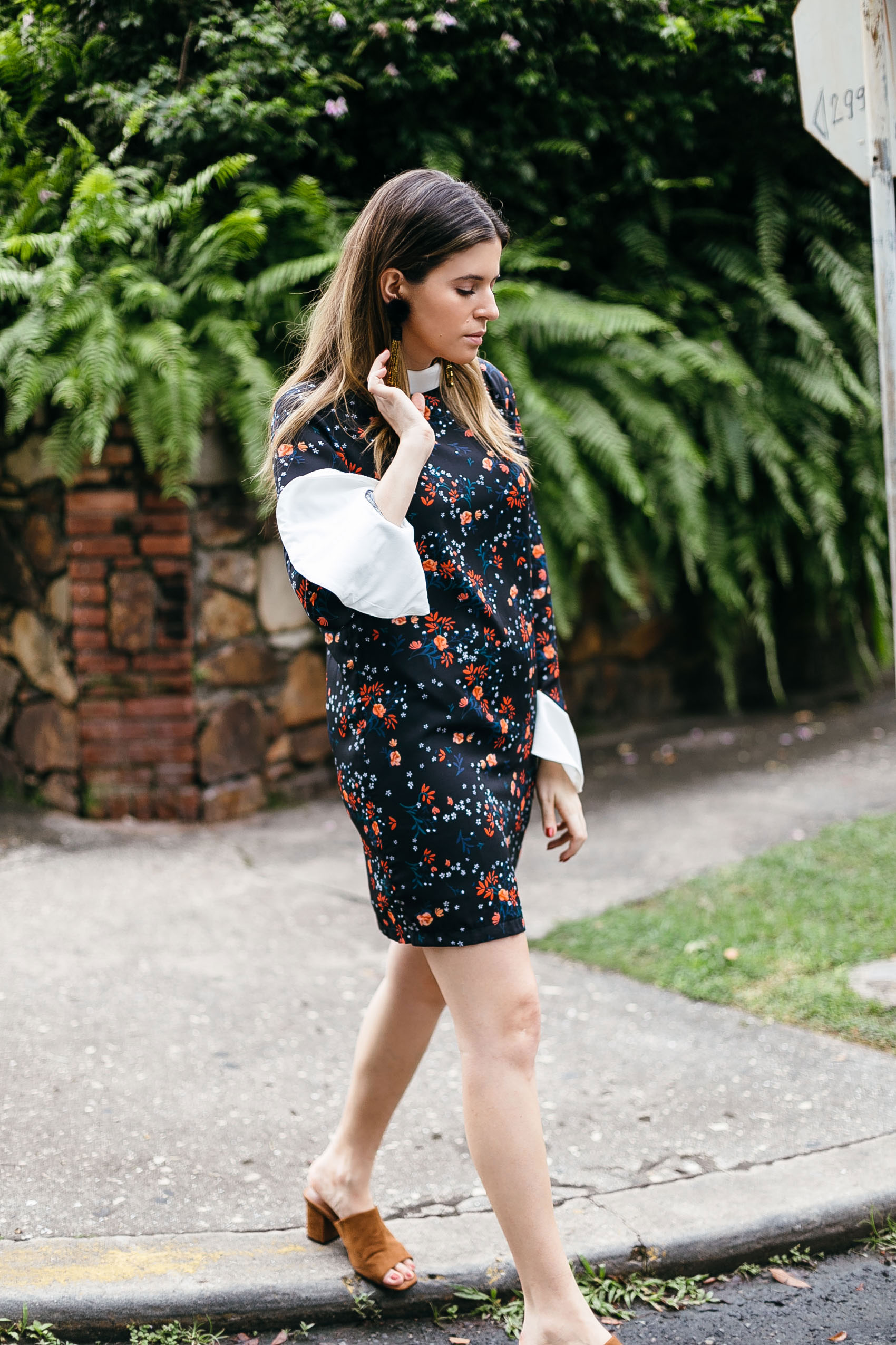 Maristella wearing a floral tunic dress with contrast flared sleeves, mules and tassel earrings