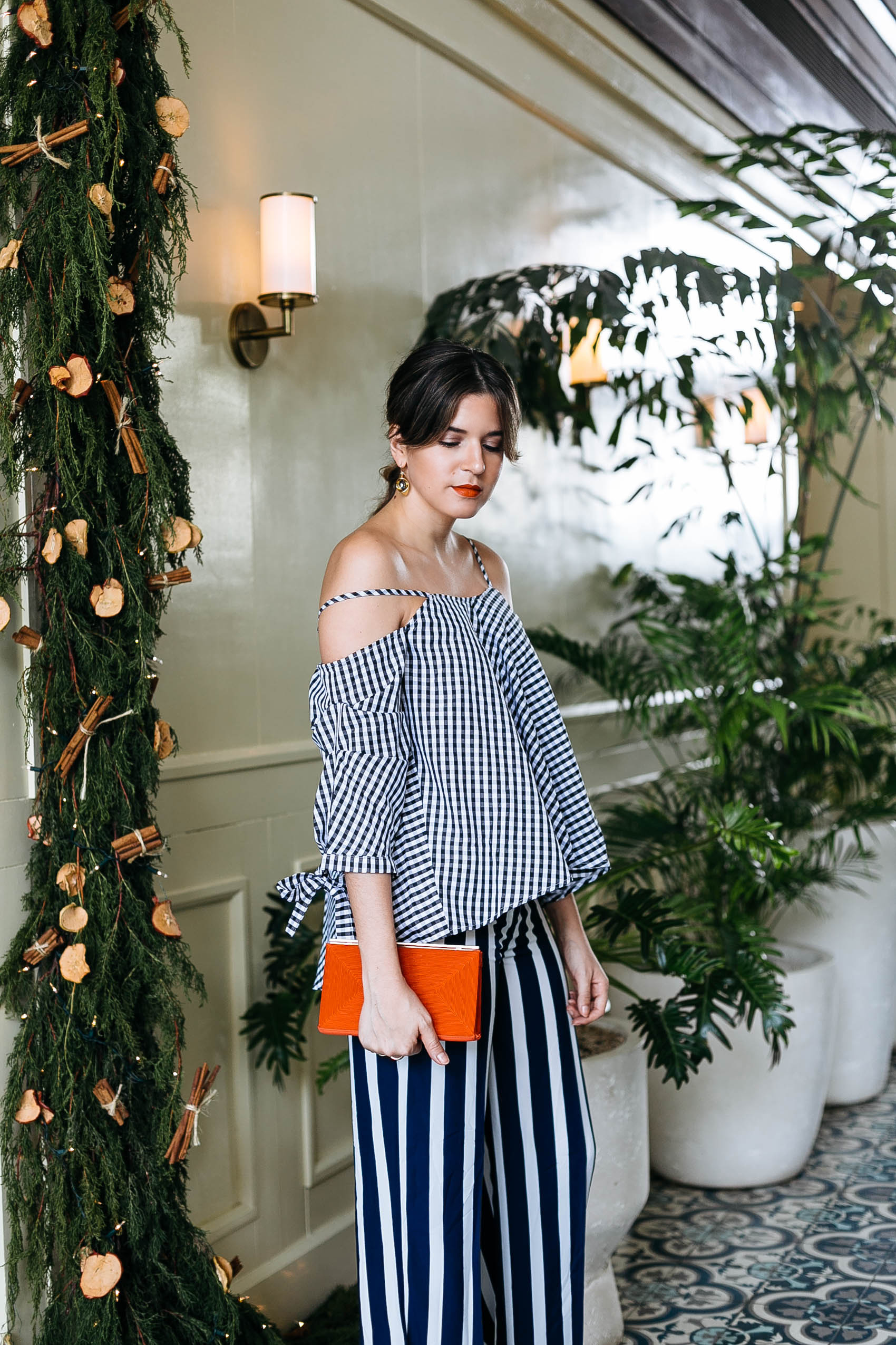 Maristella wears a gingham cold shoulder blouse with wide stripe pants and a red satin clutch for Christmas