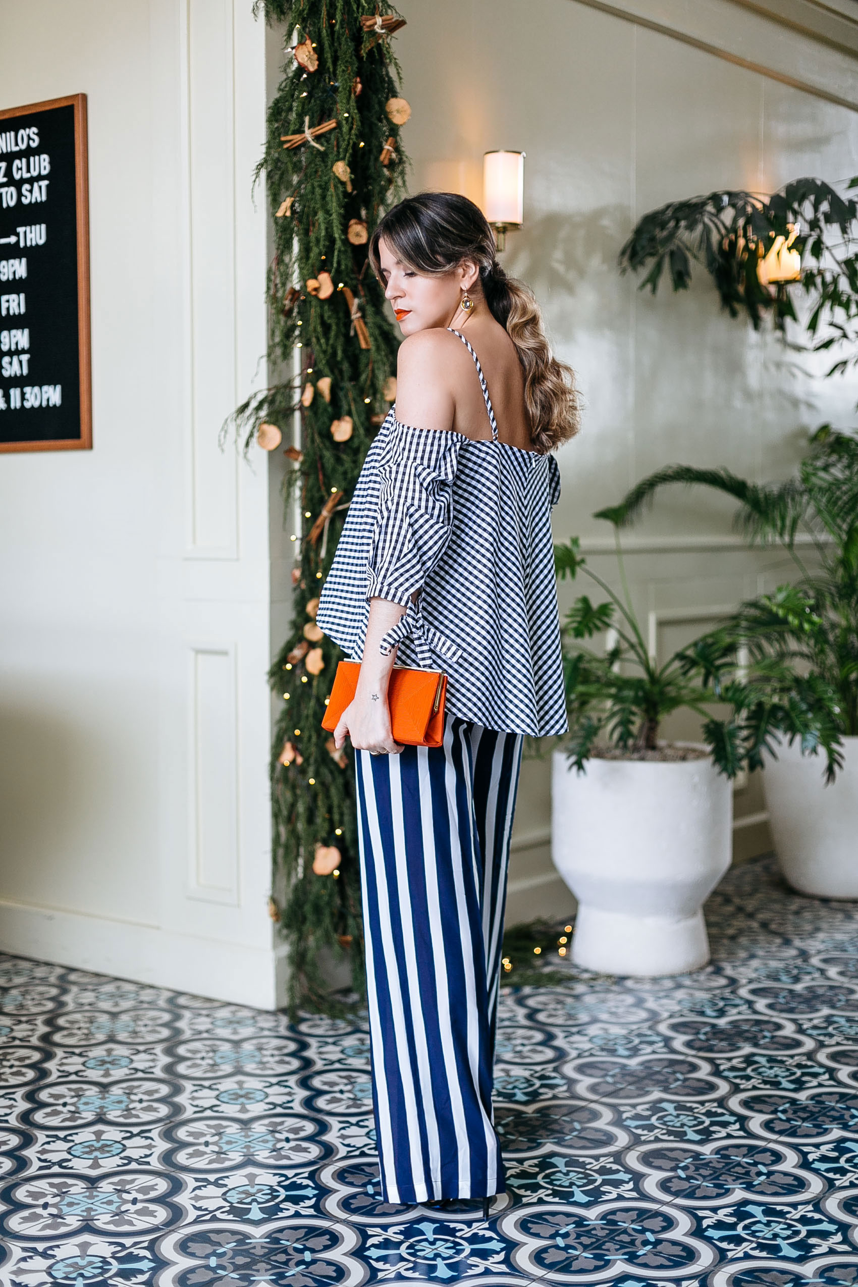 Maristella at the American Trade Hotel wearing a gingham blouse with stripe pants and a red clutch