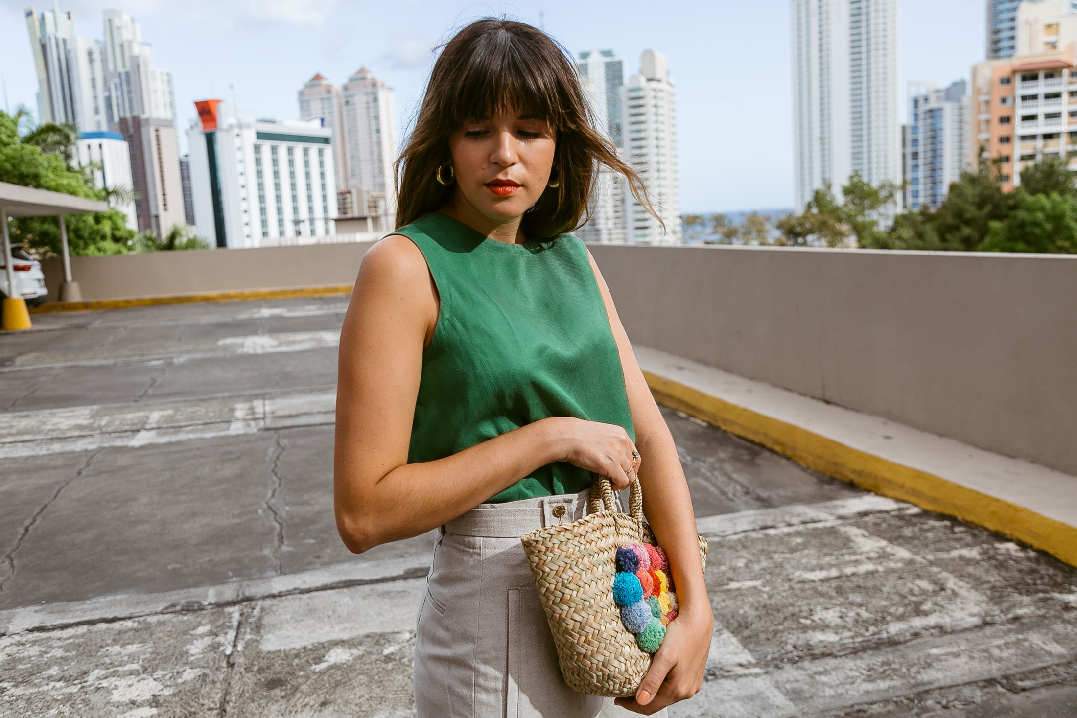 Maristella wears a small straw tote bag with colorful poms from Purificacion Garcia