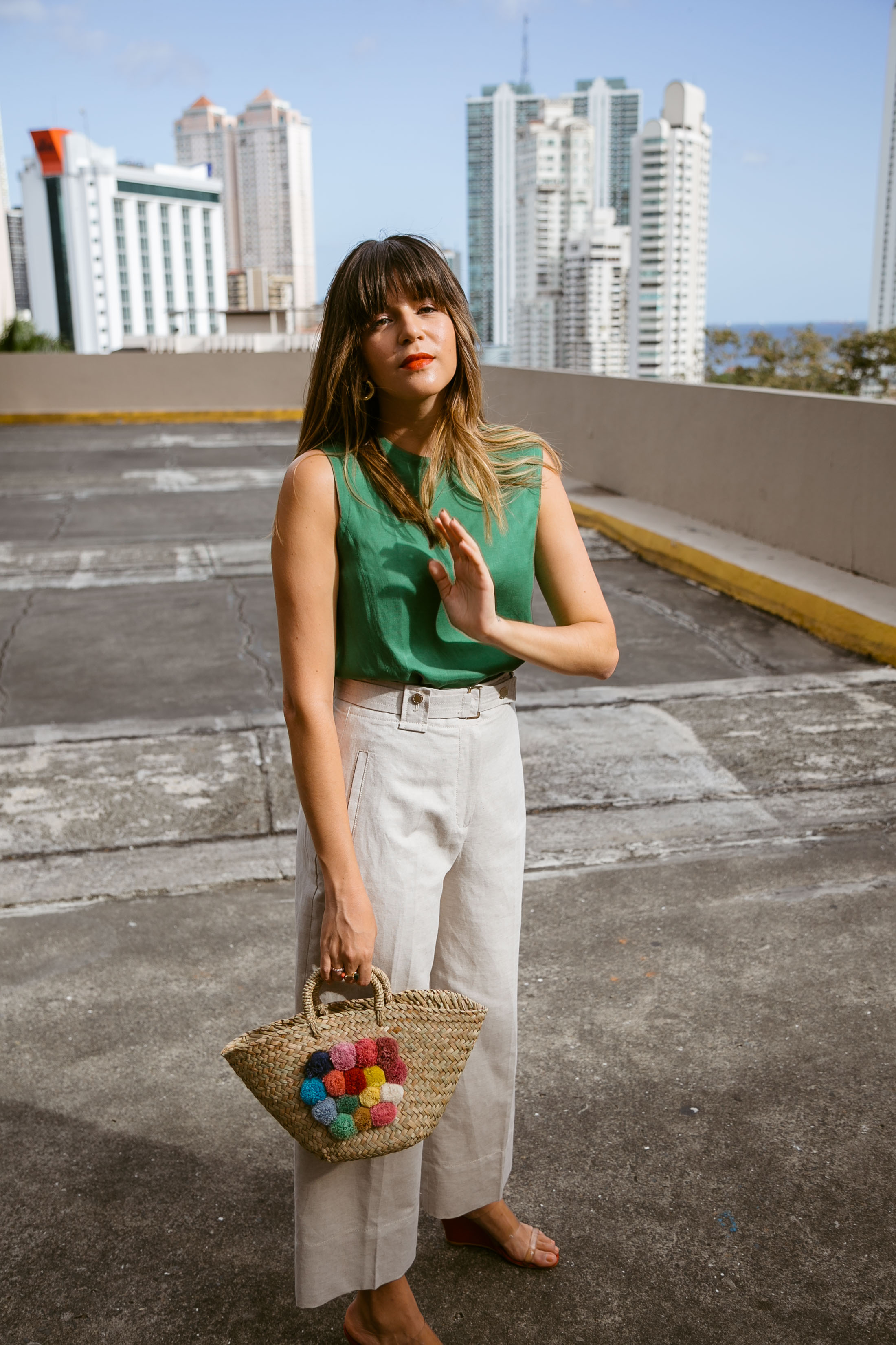 Maristella wears a green top, wide leg beige pants and straw tote bag for Spring 2017