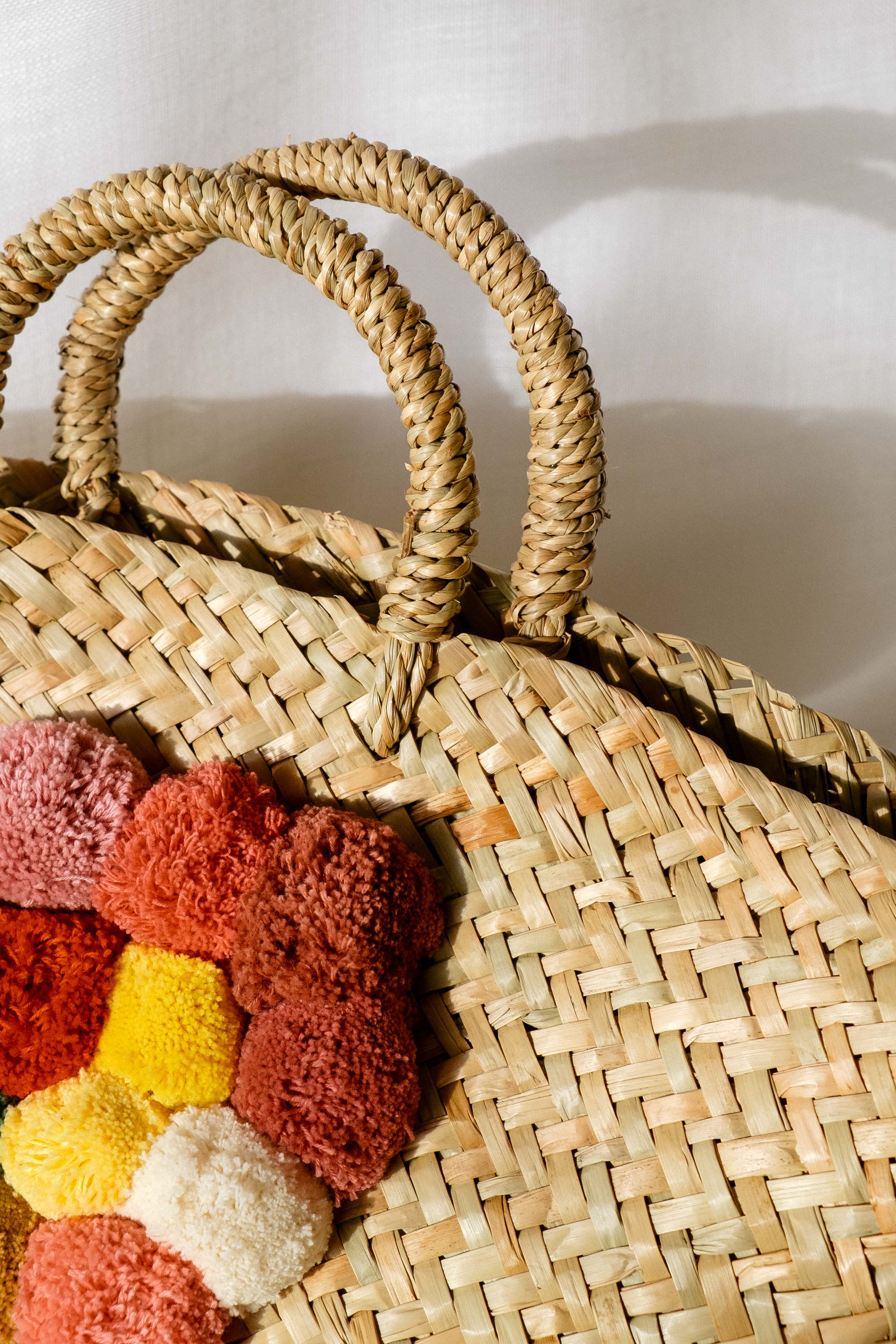 Close up weave detail of a Purificación García straw bag with poms