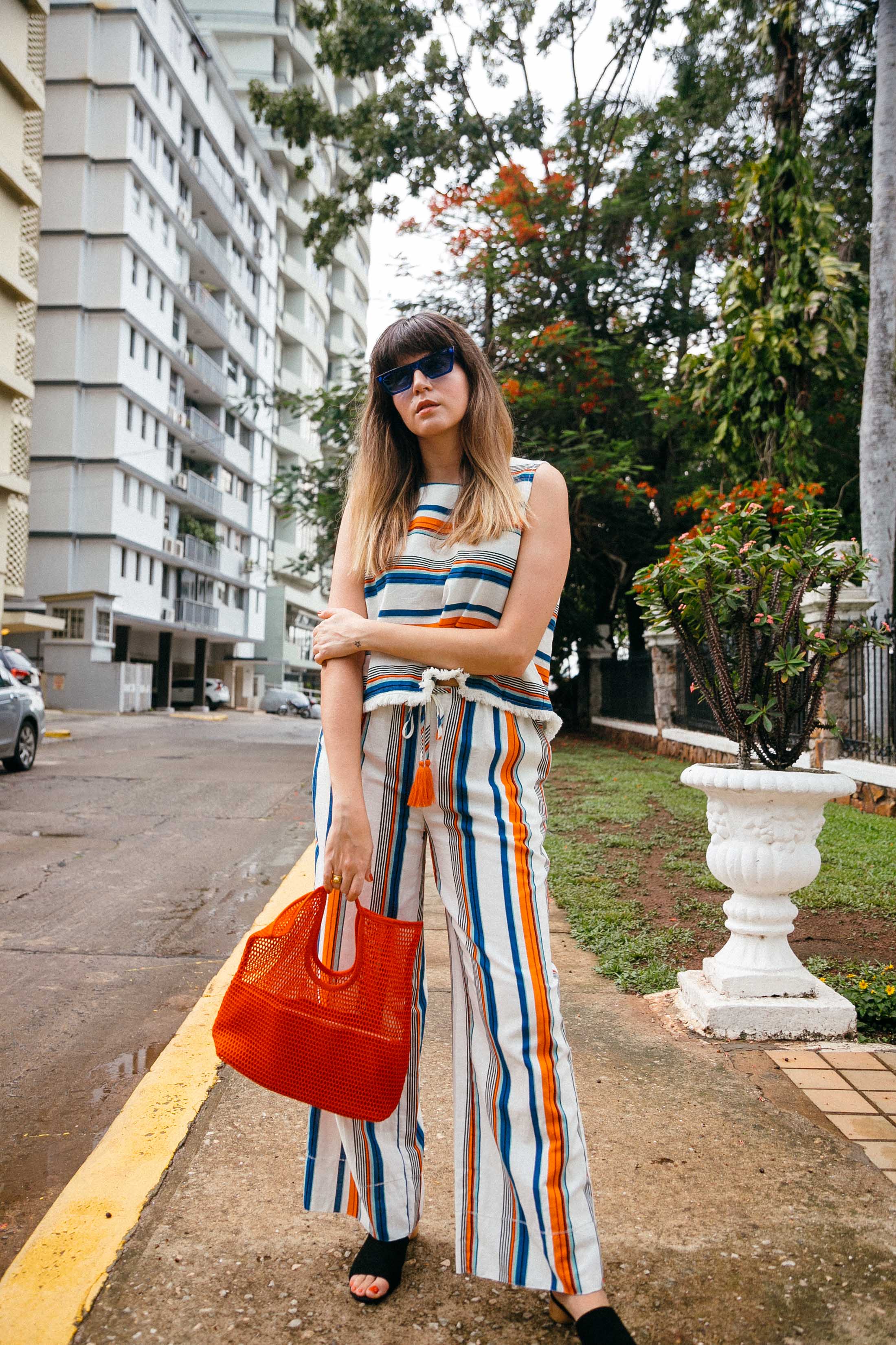 Maristella wears a stripe matching set from Moon River, black suede mules from Mango, red net tote bag from COS, blue sunglasses from Mango