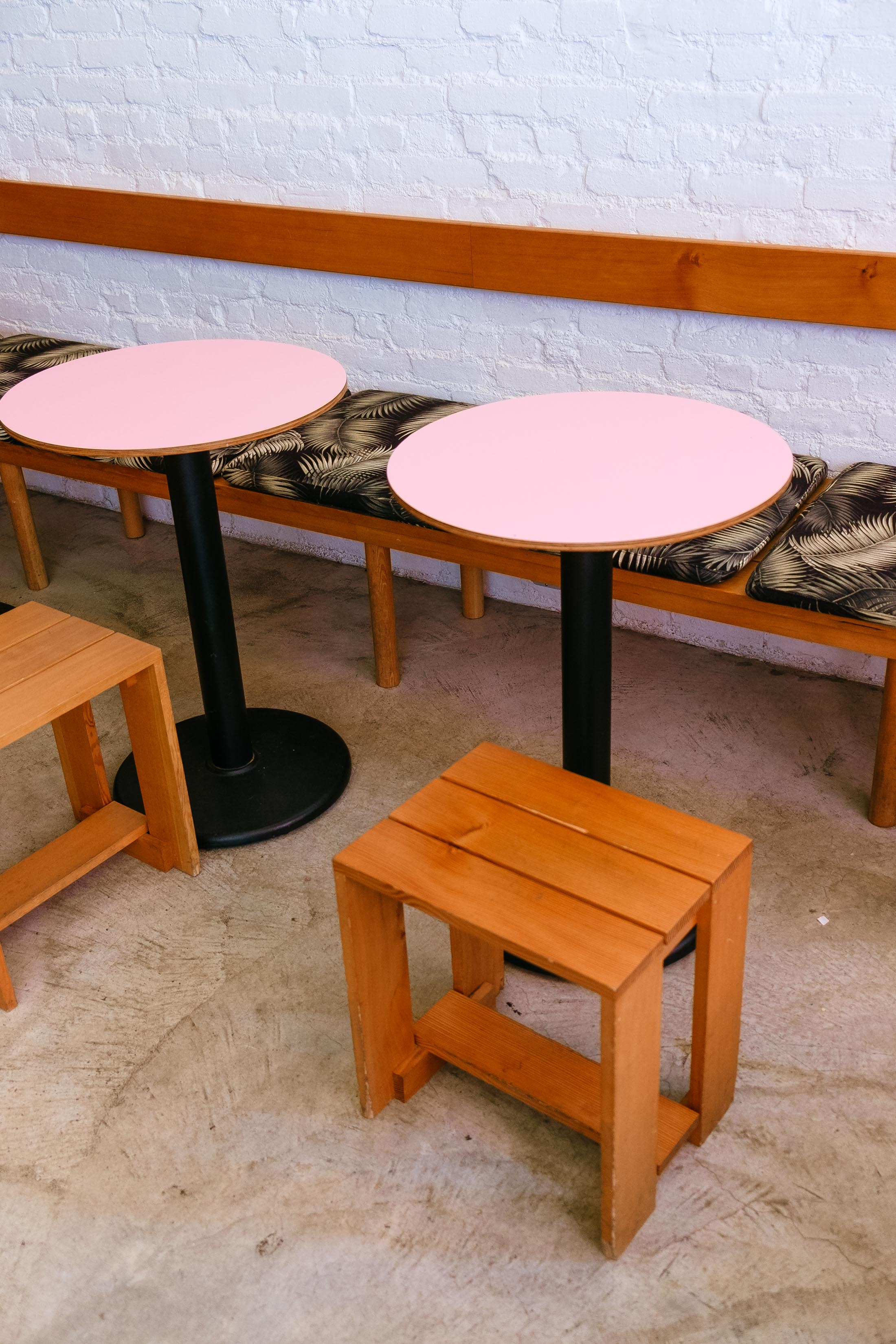 Round pink tables, wooden stools and palm print cushions at Cha Cha Matcha