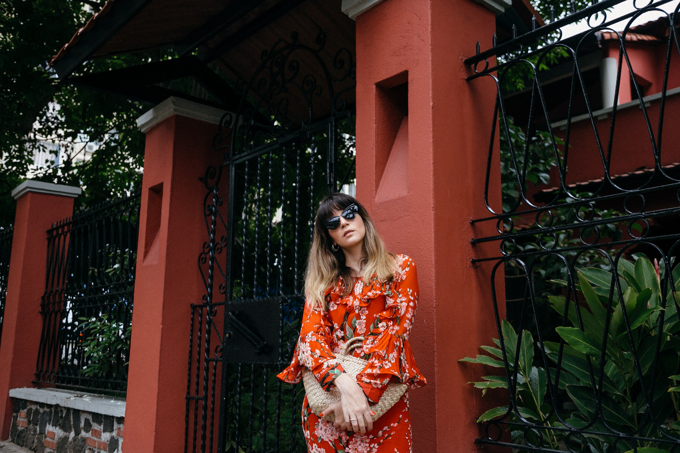 Maristella wears a red floral dress and straw bag