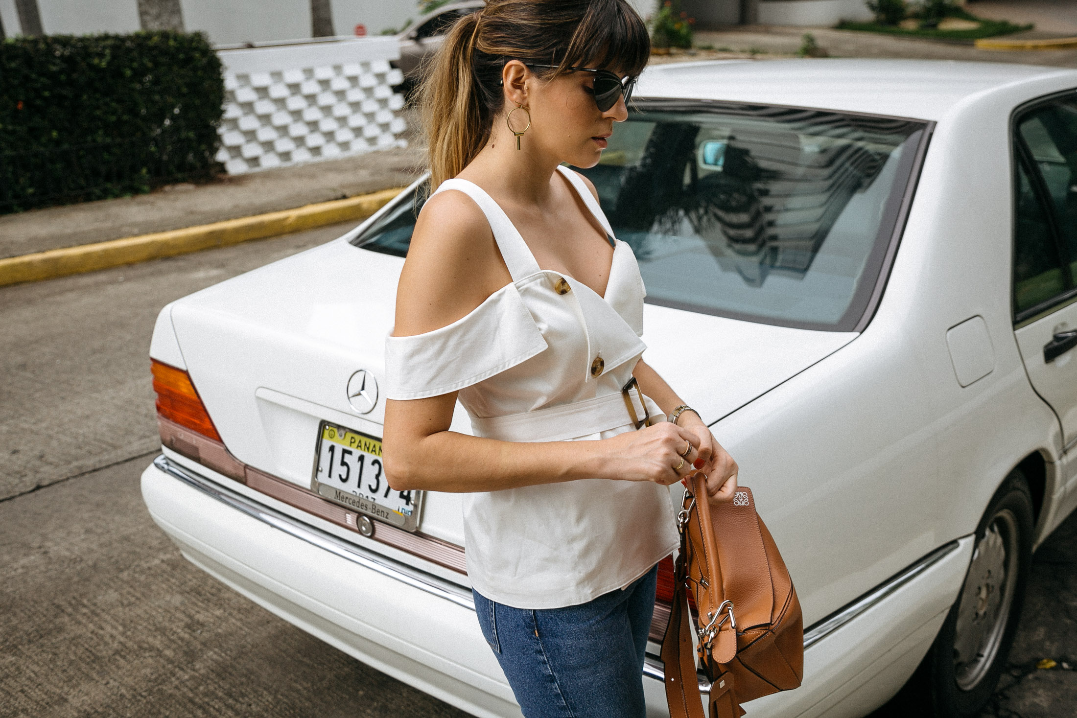 Maristella wears an off the shoulder white top from C/meo, jeans and a brown leather bag from Loewe