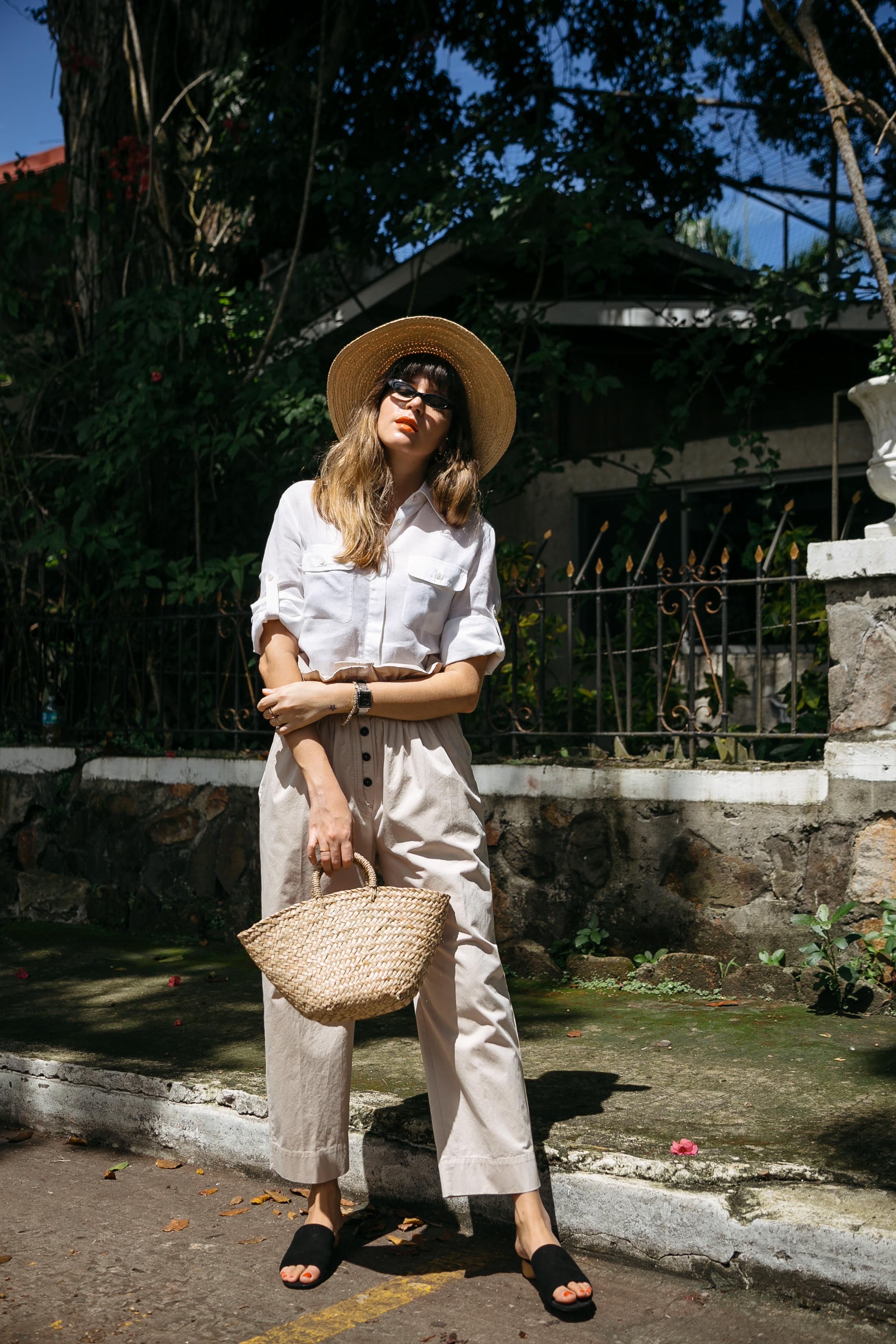 Maristella in a South of France inspired look with a straw hat, white button down shirt and khaki paper bag pants from Mango