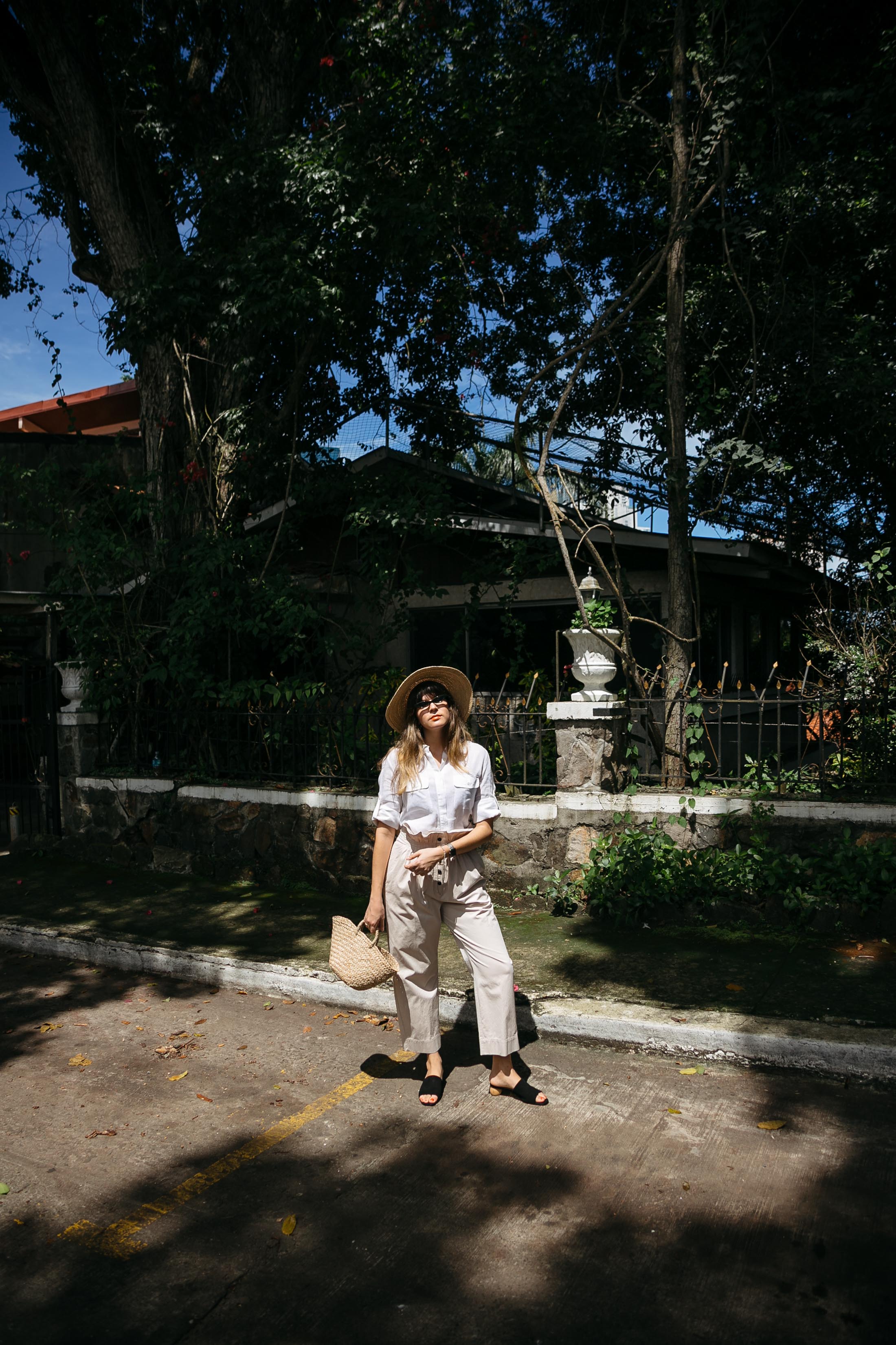 Maristella wears paper bag khakis from Mango with a white linen cargo shirt, Mango suede mules, a straw bag and wide brim hat.