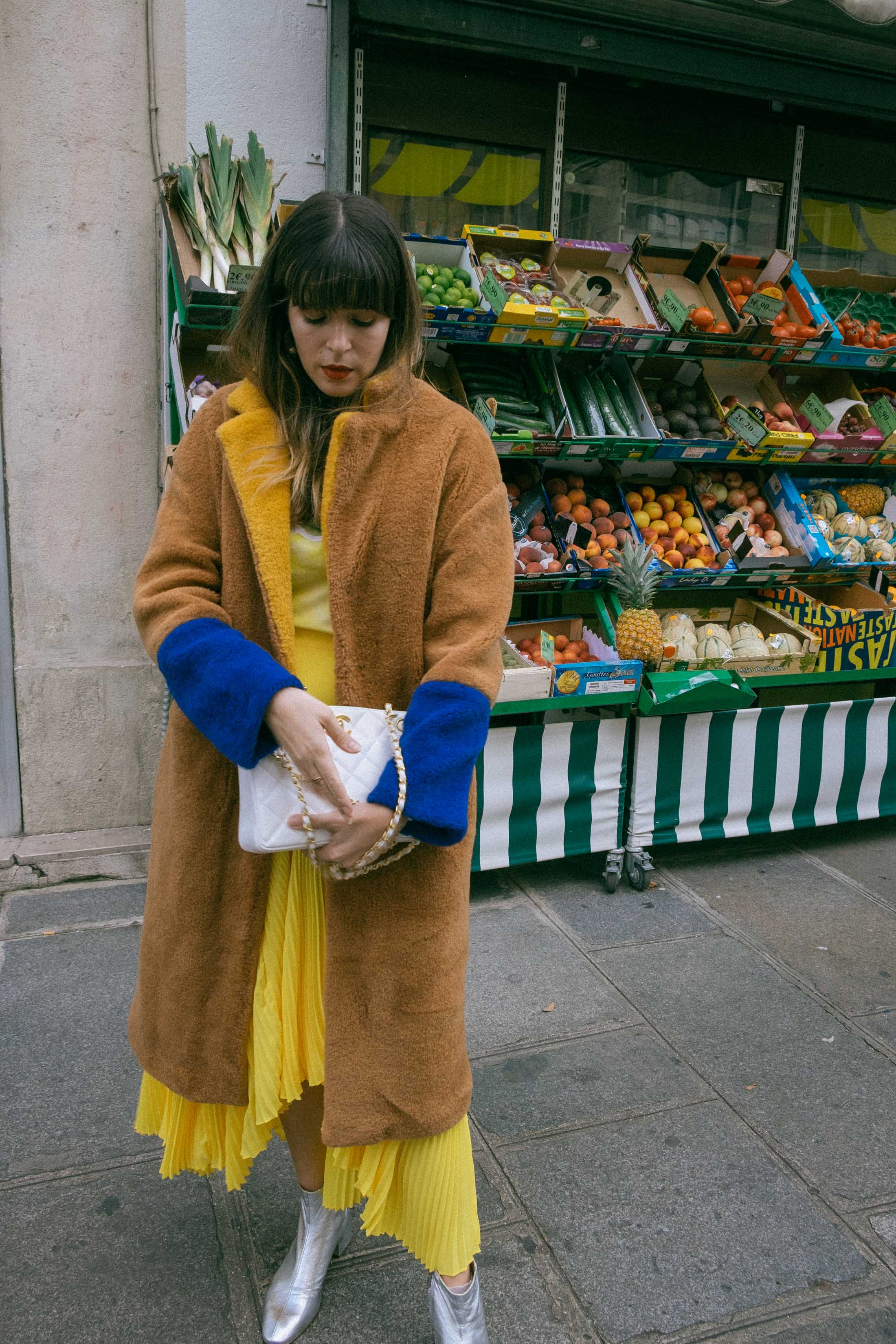 Maristella wears a brown teddy coat with contrast blue sleeves and yellow collar from Mango, white Chanel vintage bag, Loeffler Randall silver boots, yellow pleated skirt and Ganni lemon t-shirt